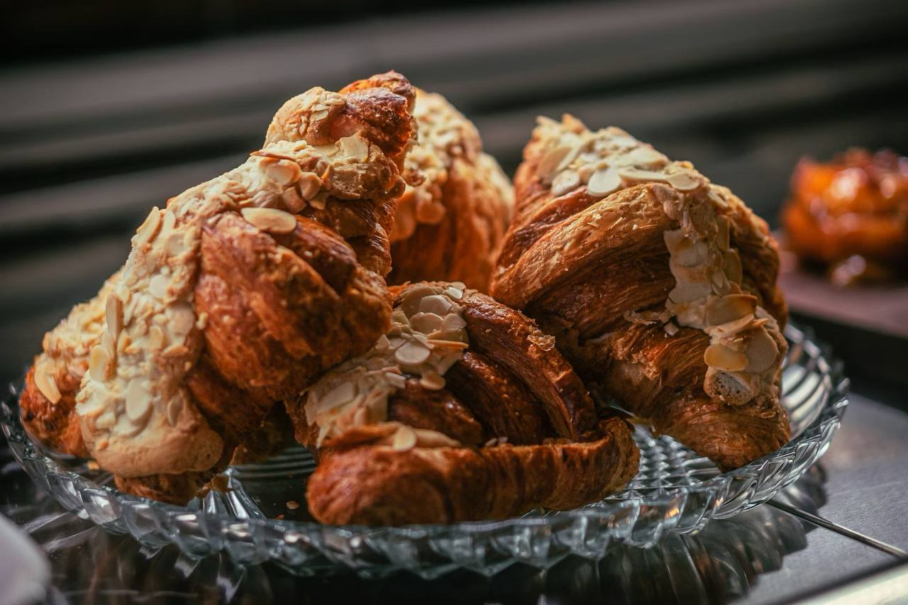 Freshly baked almond croissants topped with sliced almonds, on a glass dish.