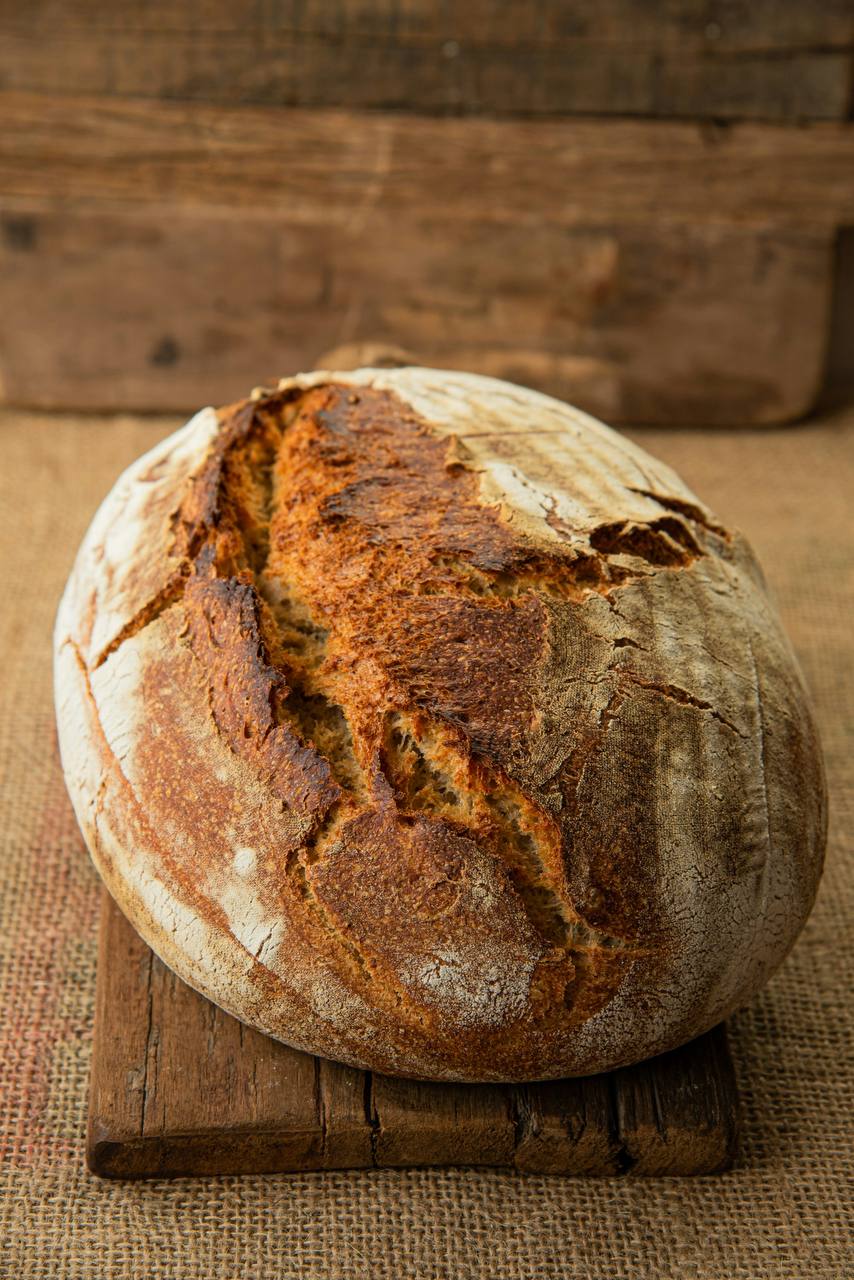 A rustic sourdough country loaf with a dark crackling crust, resting on a wooden board.