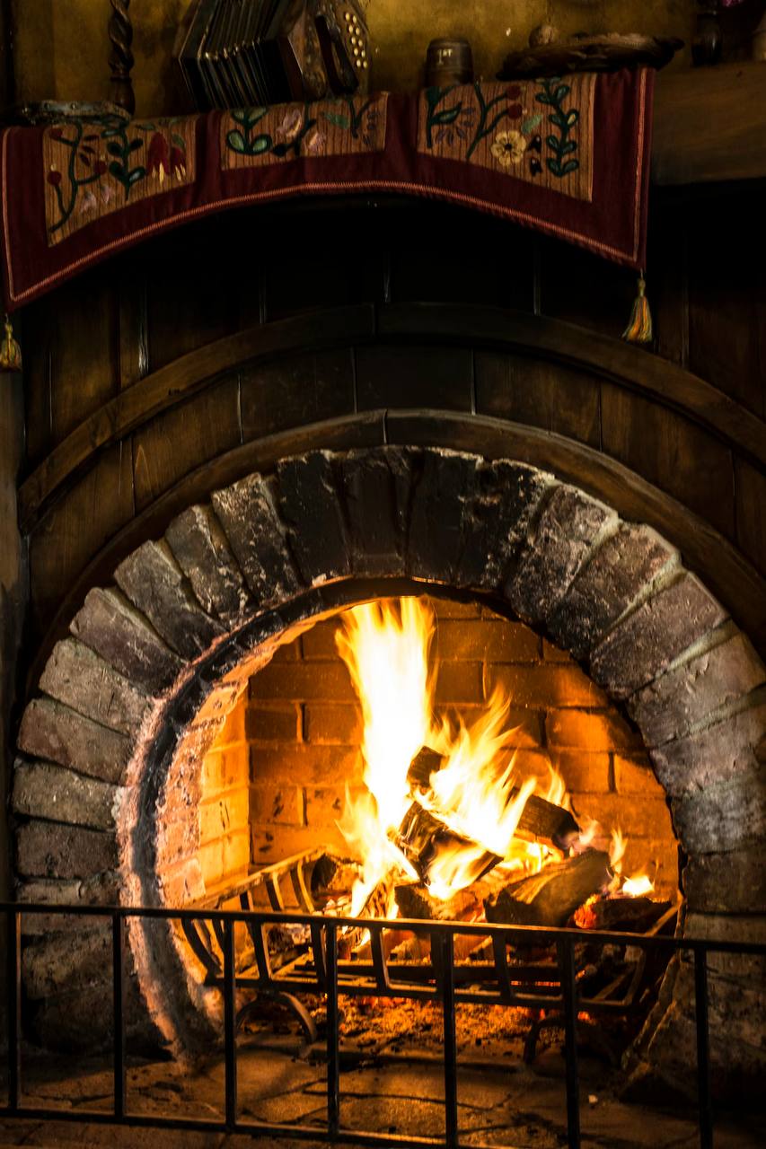 Embers and Oak hero photograph — a stone wood-fired hearth with a live fire burning