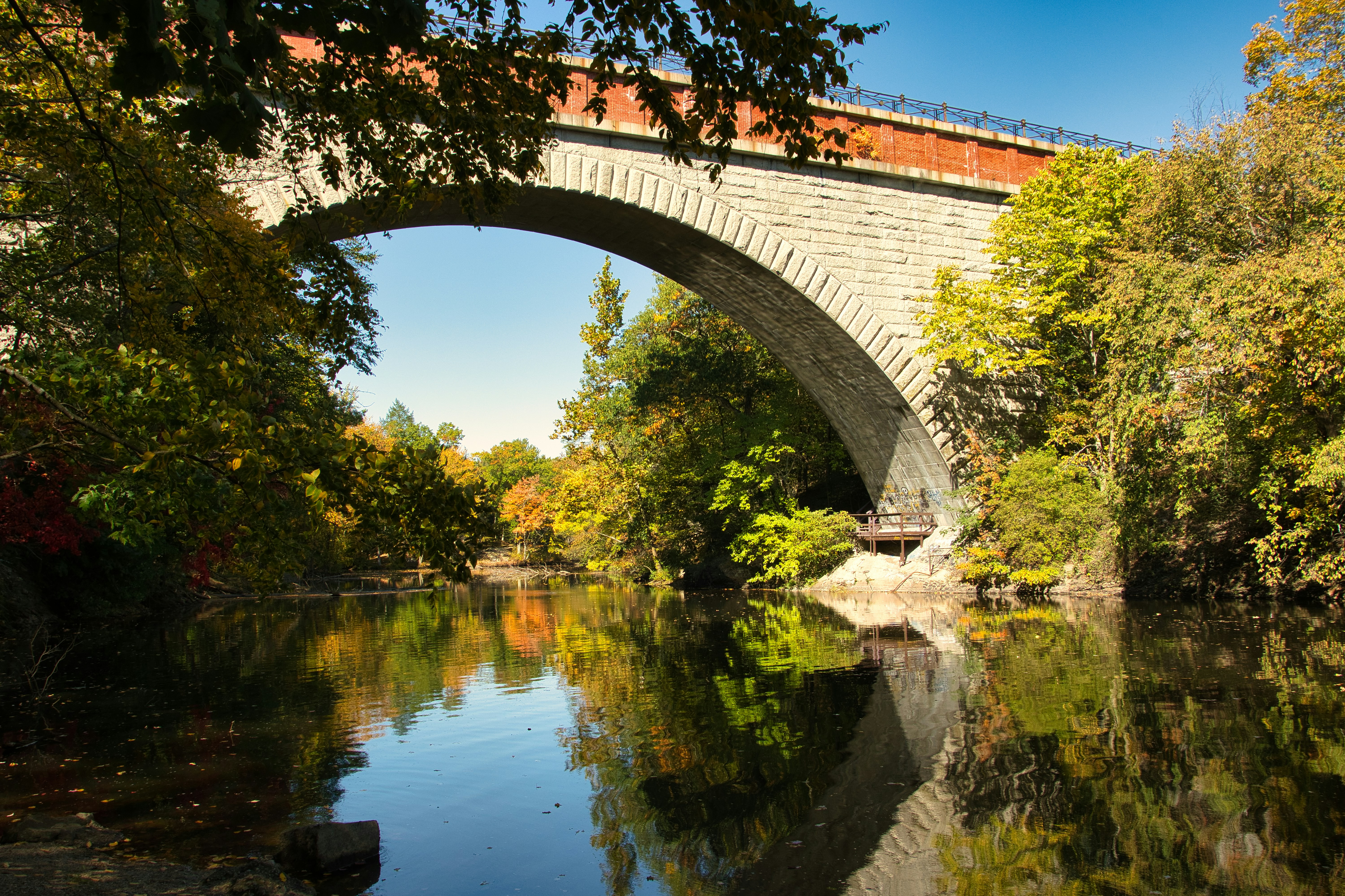 A stone arch bridge spanning a river surrounded by autumn foliage -- the timeless New England landscapes that define the Farmington Valley.